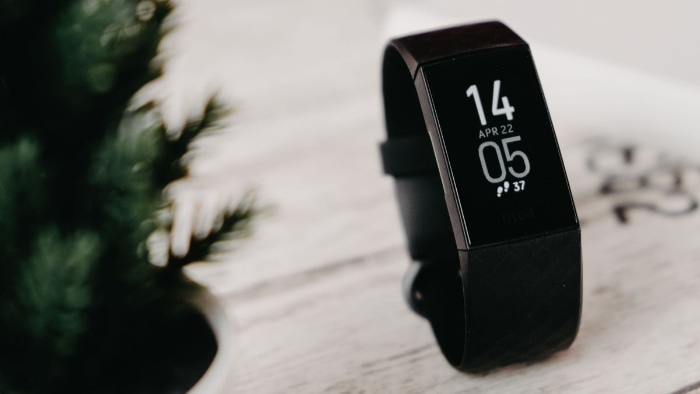 A black Fitbit fitness tracker showing time and date on a wooden surface