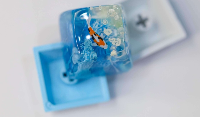 A close up of a transparent blue keycap with a koi fish design