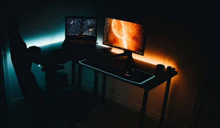 A dimly lit home office with dual monitors displaying space themed wallpapers
