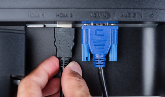 A hand inserts an HDMI cable beside a VGA cable