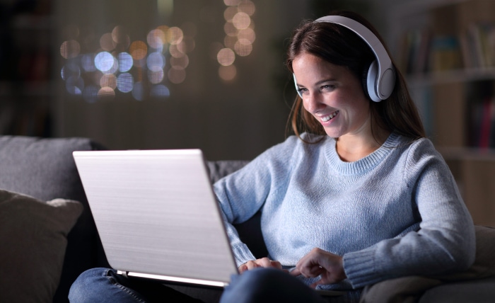 A happy woman with headphones using a laptop in a cozy room