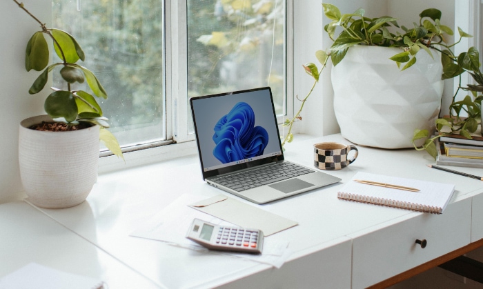 A laptop on a white desk by a sunny window