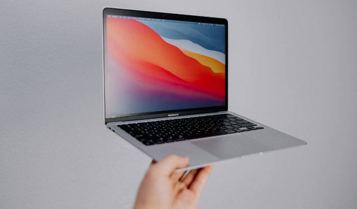 A person holding a MacBook Air with a colorful wallpaper on the screen