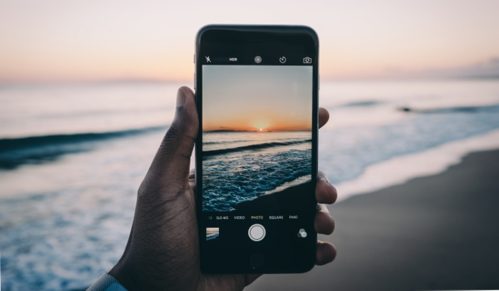 A persons hand holding a smartphone capturing a beach sunset