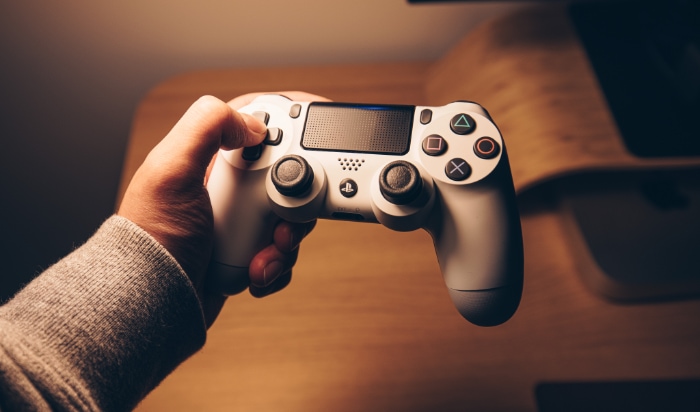 A persons hand holding a white gaming controller against a warm background