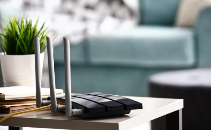 A router with three antennas on a side table near a potted plant