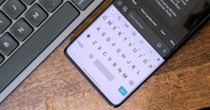 A smartphone displaying an on screen keyboard next to a physical keyboard