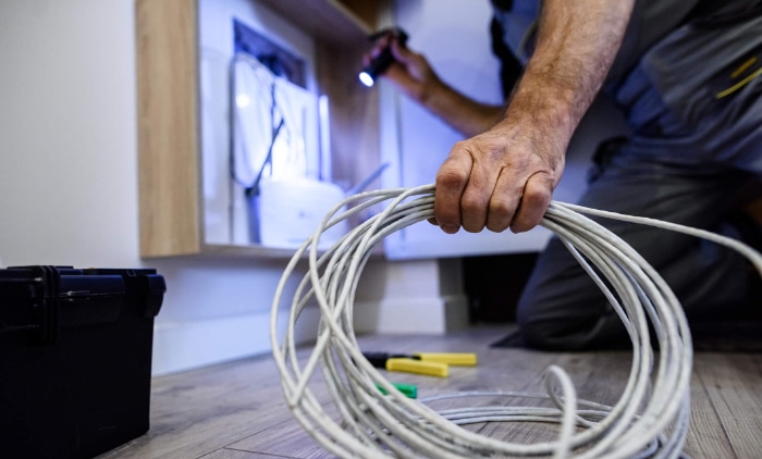 A technician holds a bundle of Ethernet cables near a wall outlet