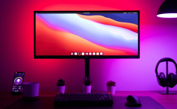 A vibrant home workspace with a monitor illuminated by purple and red smart lighting