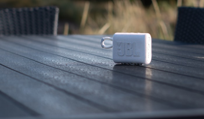 A white JBL portable speaker on a dewy outdoor table