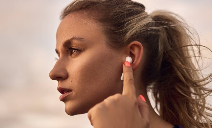 A woman touching her white earbud while looking to the side