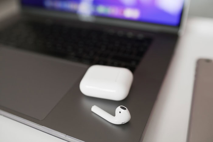 AirPods case and earbud resting on a laptop