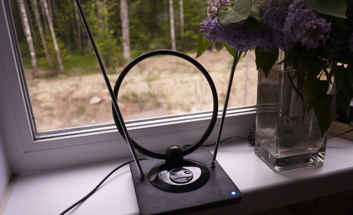 An indoor digital antenna placed on a windowsill beside a vase of lilacs