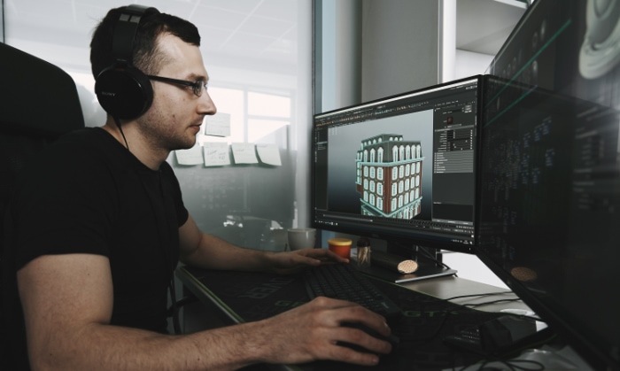 Animator working on 3D modeling of a building on a dual monitor setup