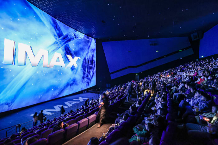 Audience watching movie screen in crowded IMAX theater