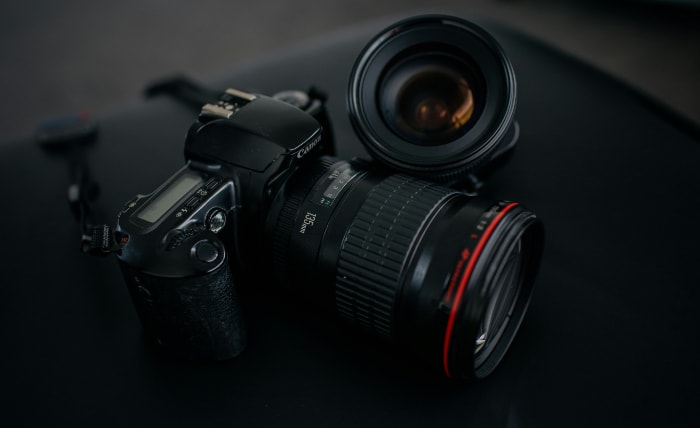 Black Canon DSLR camera with red striped lens on dark background