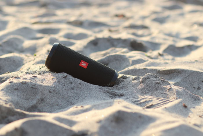 Black JBL Flip speaker on a sandy beach