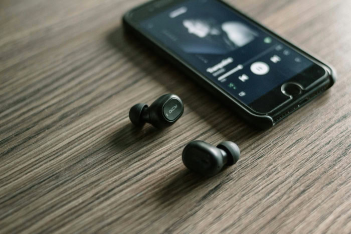 Black QCY wireless earbuds on wooden table near smartphone