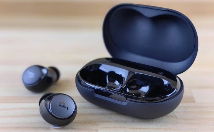 Black TWS earbuds in open charging case on wood