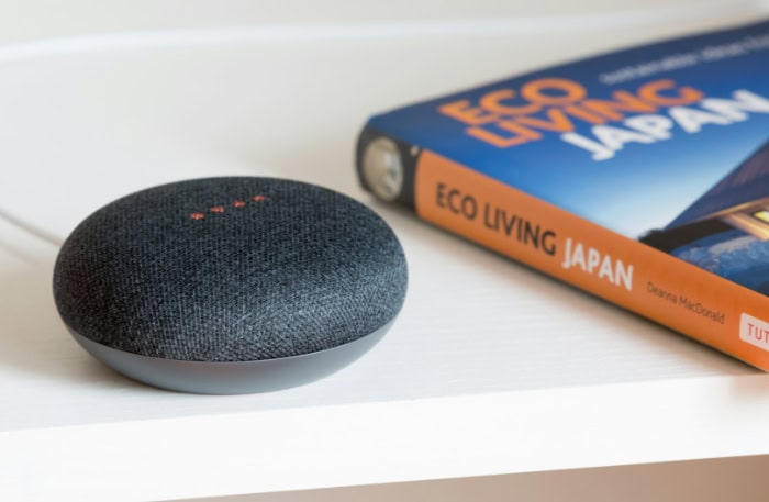 Black smart speaker on a white shelf near book