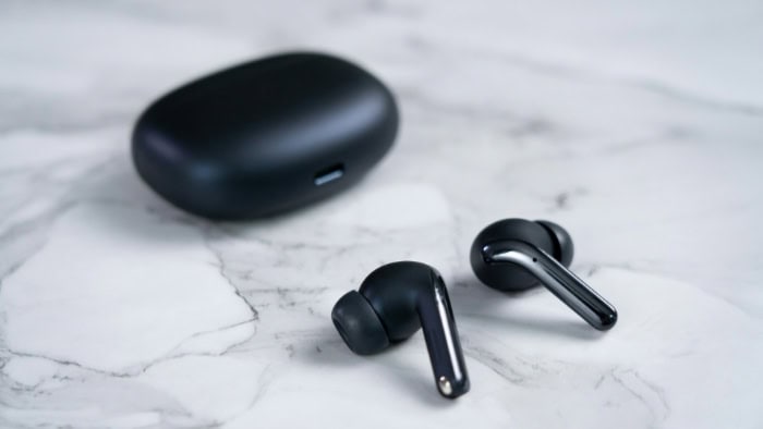 Black wireless earbuds with charging case on marble surface