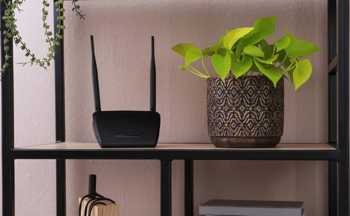 Black wireless router on shelf with potted plant and decor