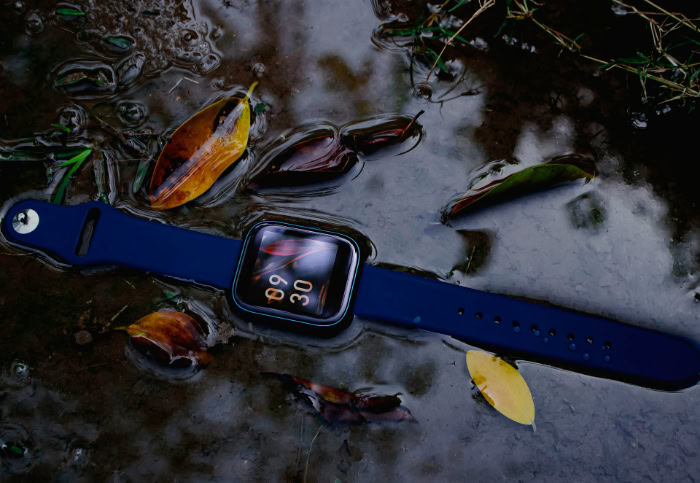 Blue waterproof smartwatch in puddle with autumn leaves