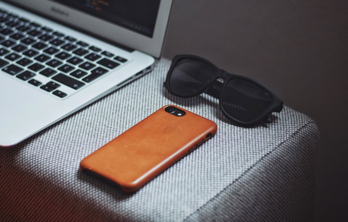 Brown leather iPhone case next to laptop and sunglasses