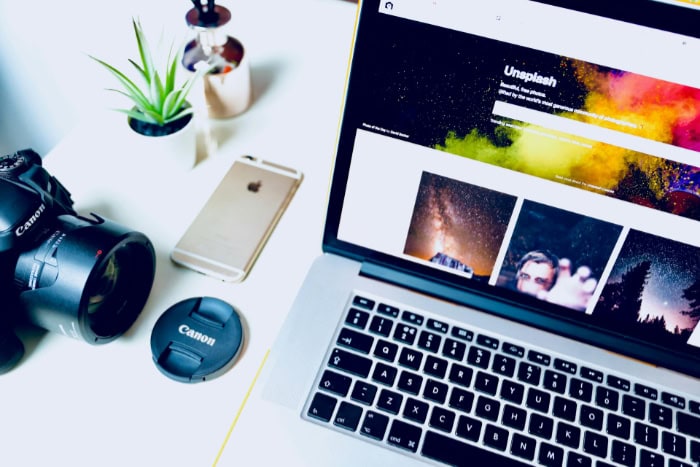 Canon camera lens beside laptop displaying Unsplash website