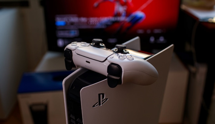 Close up of a PS5 controller resting on top of a PS5 console with Spider Man game on the background screen