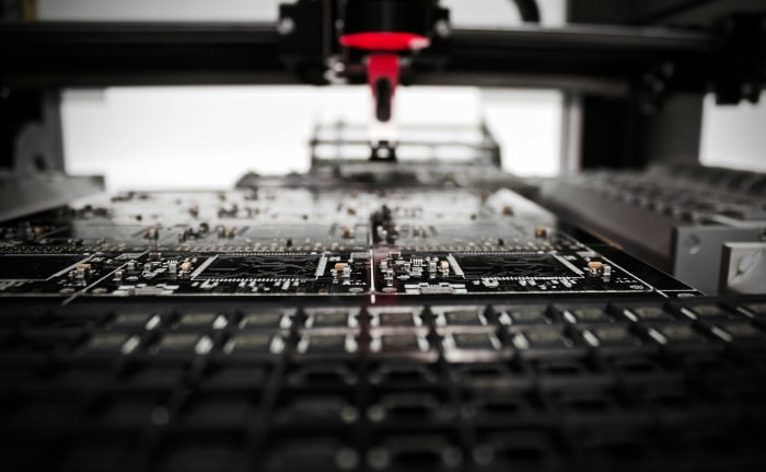 Close up of a printed circuit board in manufacturing with a red robotic arm