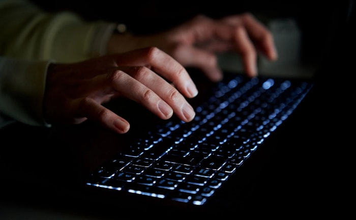 Close up of hands typing on a backlit laptop keyboard in low light