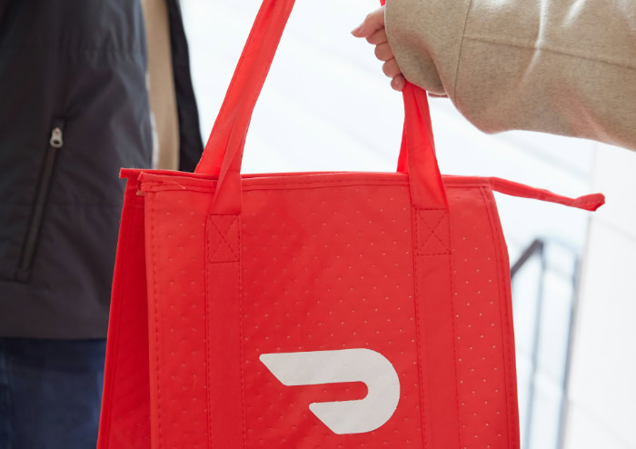 Courier handing DoorDash insulated delivery bag to customer