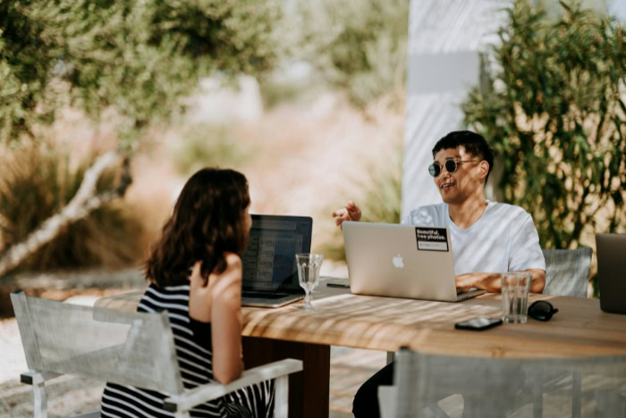 Coworkers talking outdoors with laptops on table