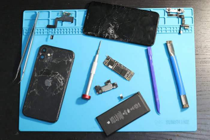 Cracked iPhone parts and repair tools on blue mat