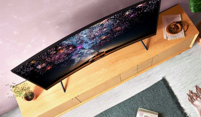 Curved TV displaying fireworks on wooden desk