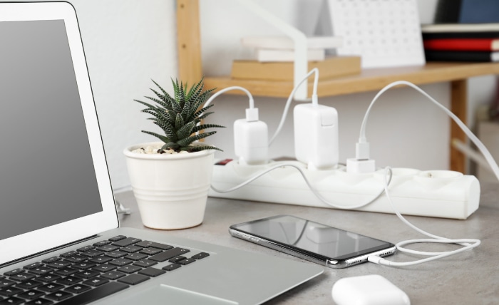 Desk workspace with laptop smartphone charging cables and plant