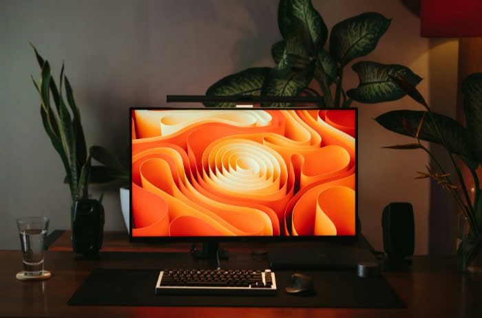 Desktop monitor displaying abstract orange shapes with plants nearby