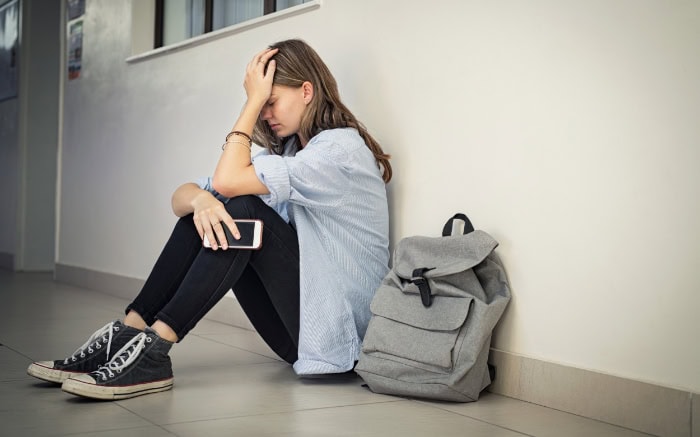 Distressed student sitting on floor with smartphone and backpack