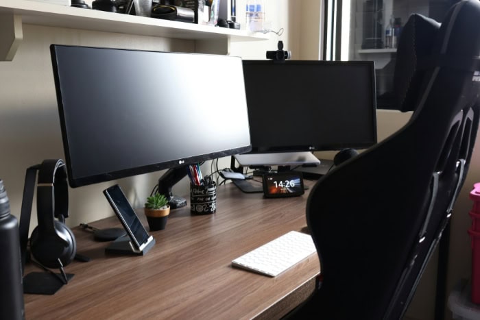 Dual monitor PC setup with gaming chair on wooden desk