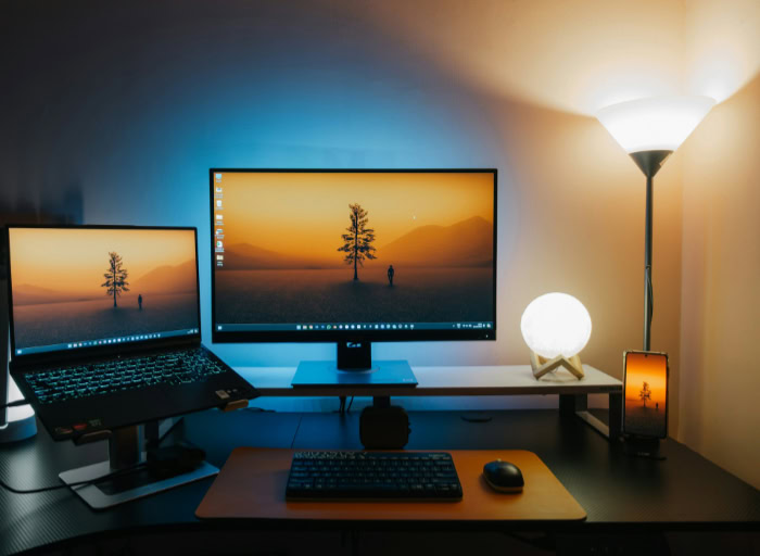 Dual monitor laptop desk setup with warm ambient lighting