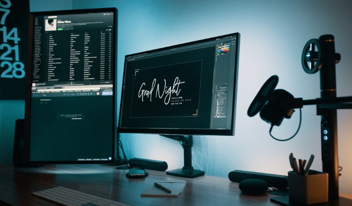 Dual monitor setup with graphic design software and music playlist