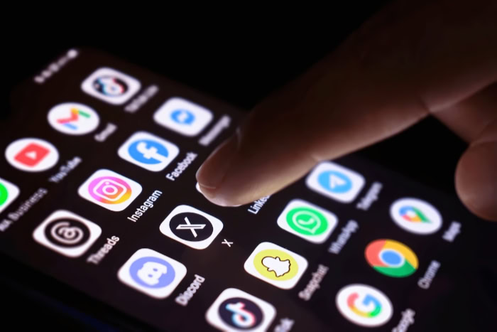 Finger selecting X app icon on smartphone screen
