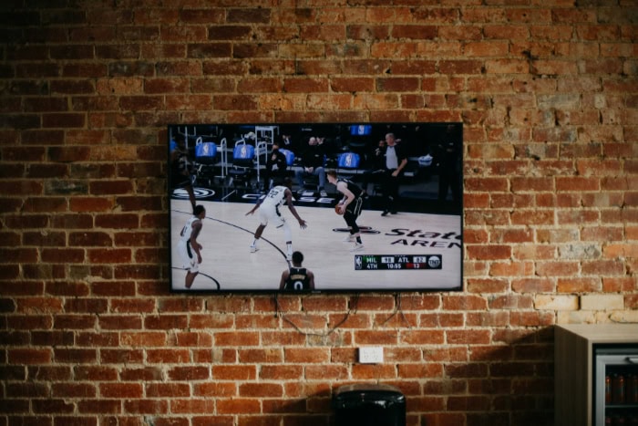 Flat TV wall mounted displaying basketball game on brick wall