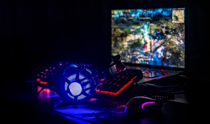 Gaming headphones illuminated by blue light resting beside a keyboard