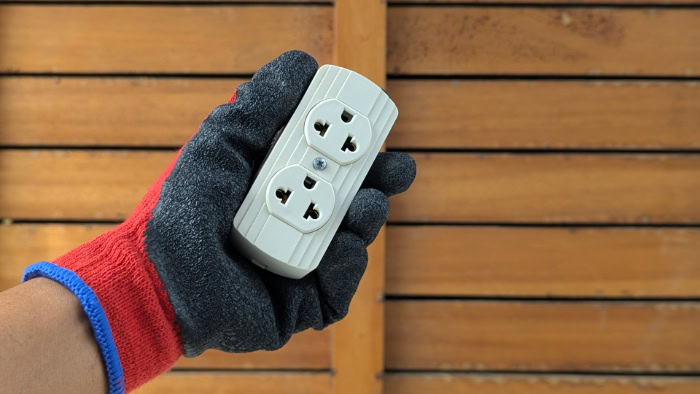 Gloved hand holding a white electrical outlet adapter