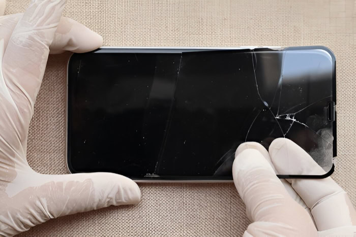 Gloved hands examining cracked smartphone screen