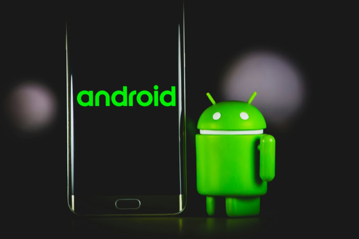 Green Android figurine next to smartphone with logo