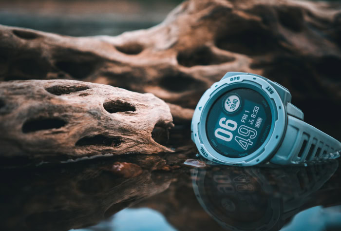 Grey Garmin smartwatch reflecting in water near driftwood