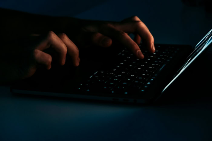 Hacker typing on a laptop keyboard in the dark